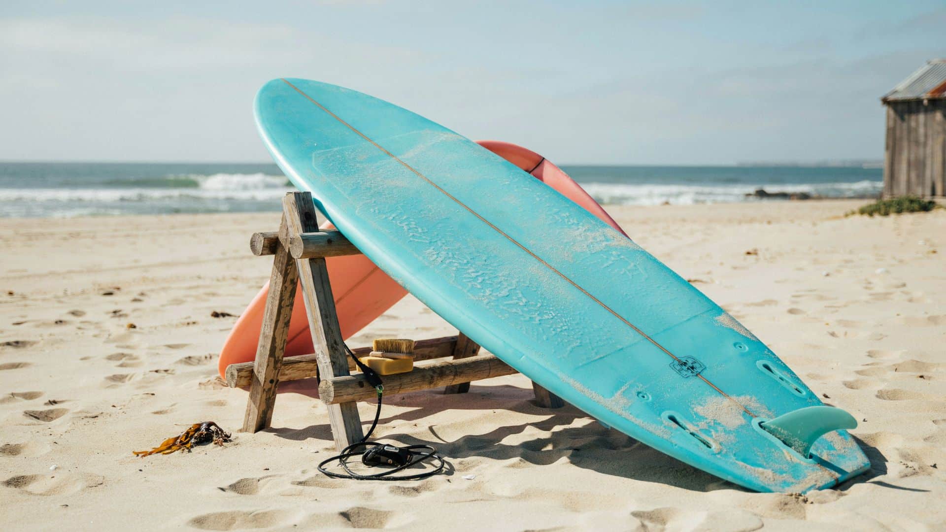Blue soft top surfboard resting on a wooden stand on a sandy beach