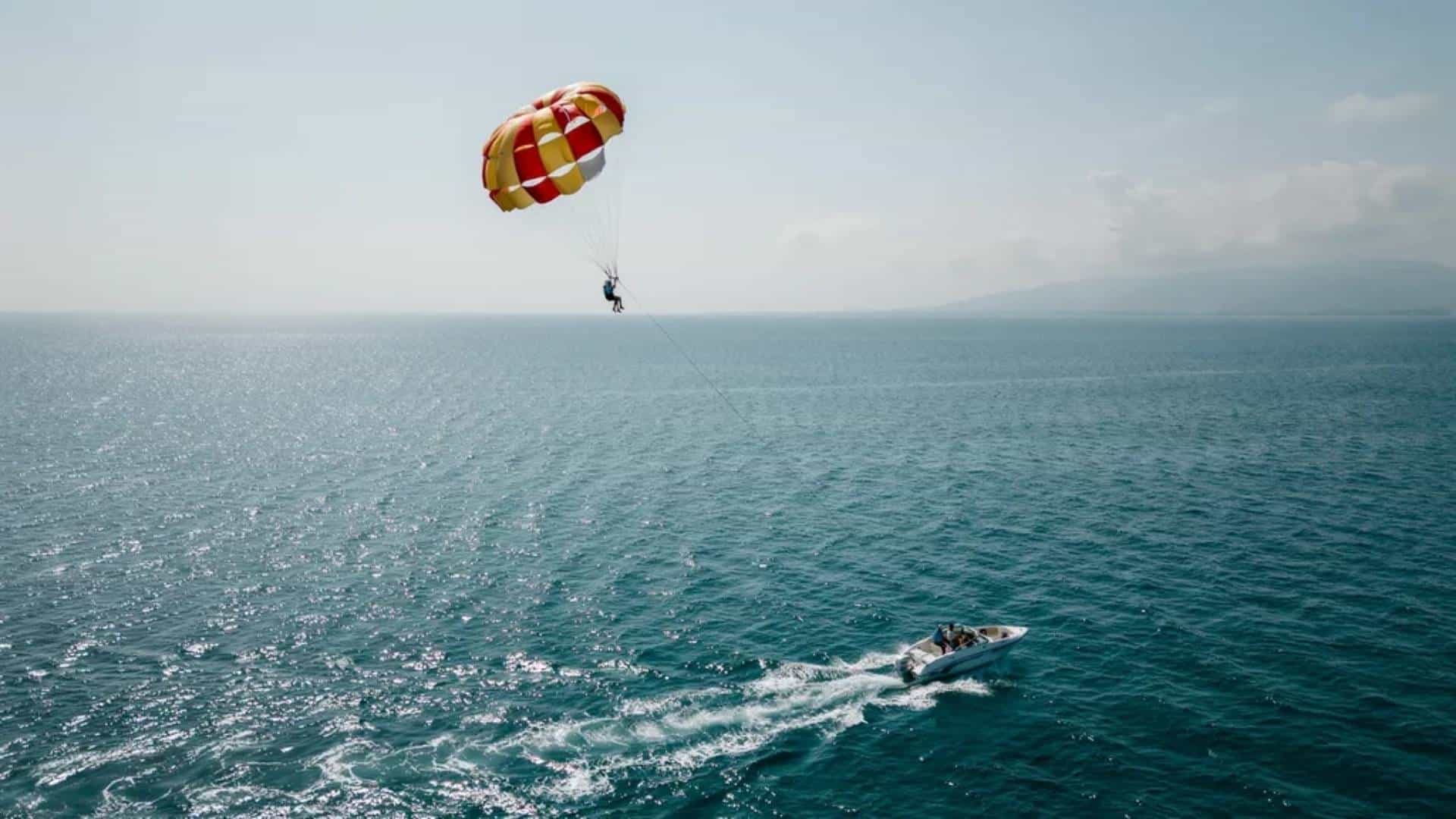 Parasailing rider floating high above ocean with boat and canopy below