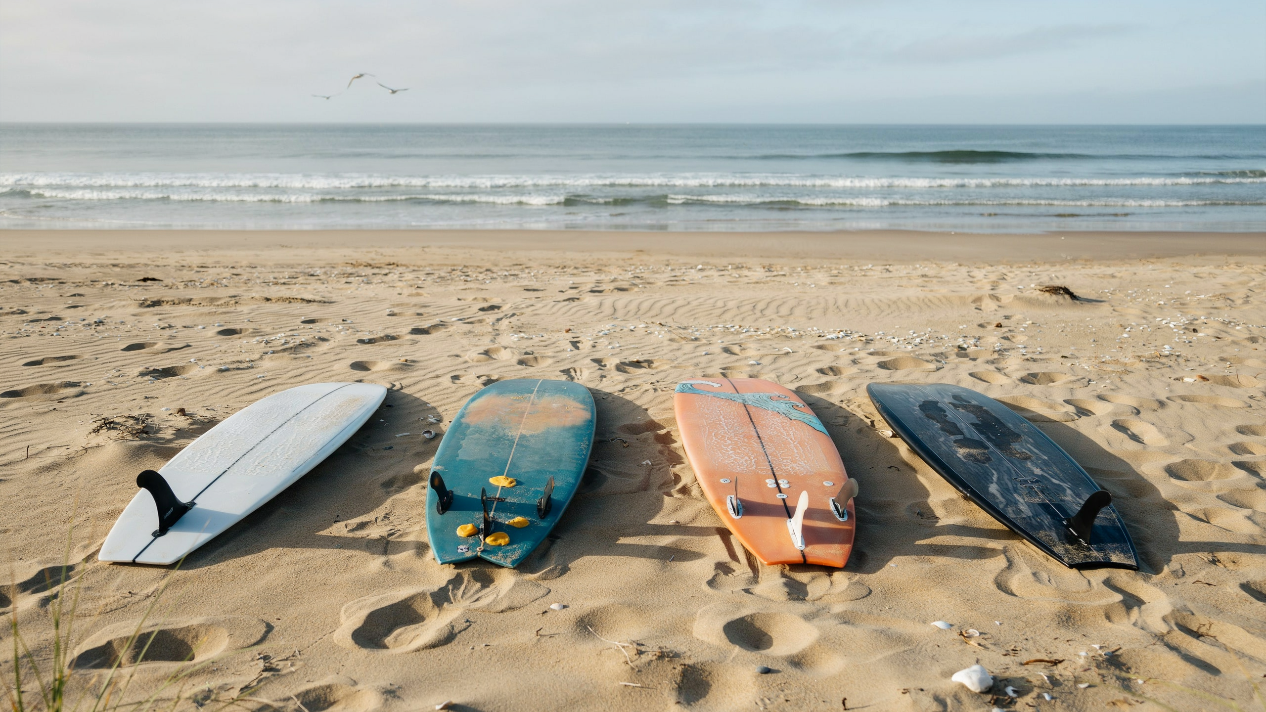 Four colorful surfboards lying on sandy beach with ocean waves in the background.