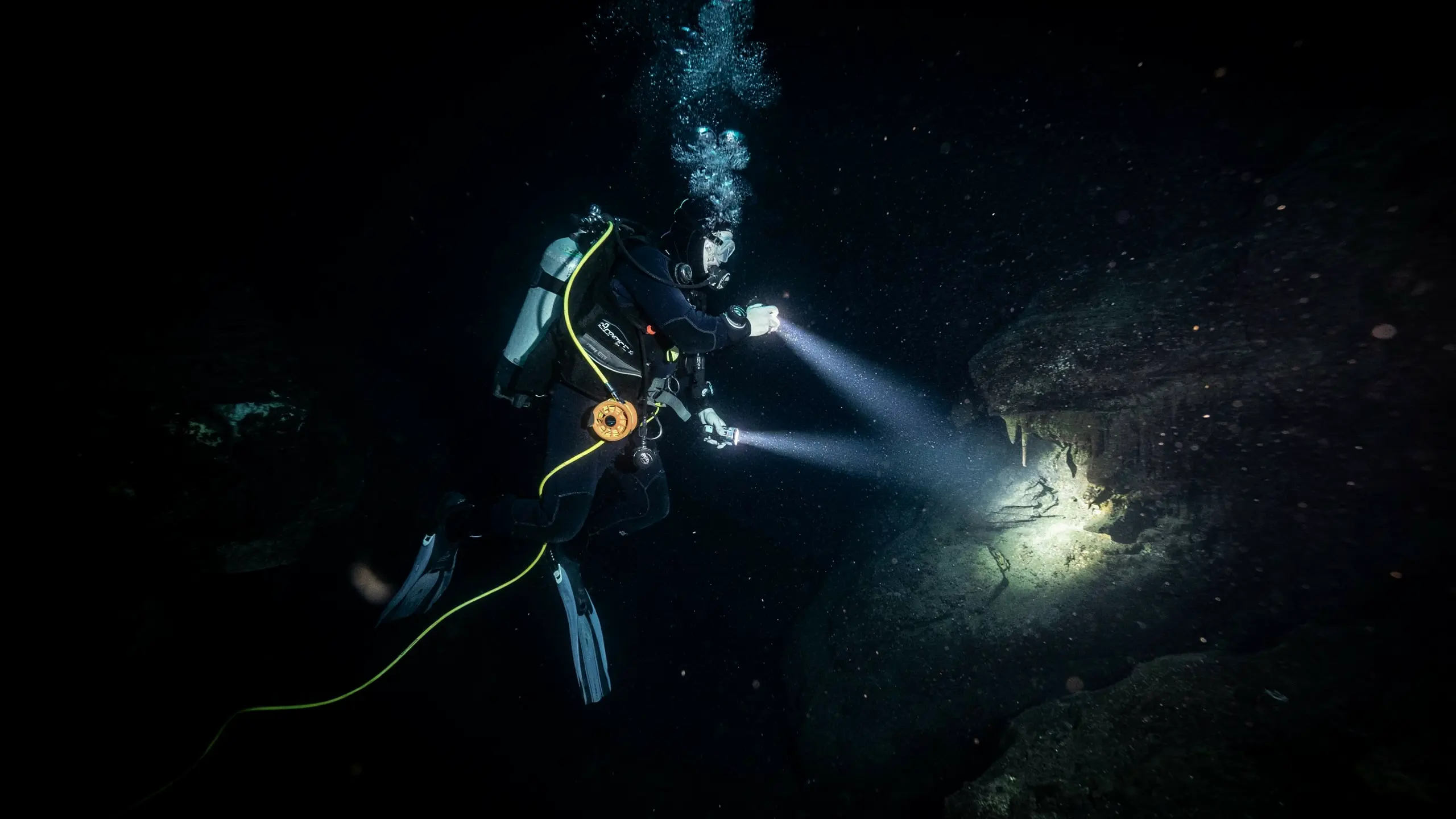 Diver inside a dark underwater cave lit only by a handheld dive light