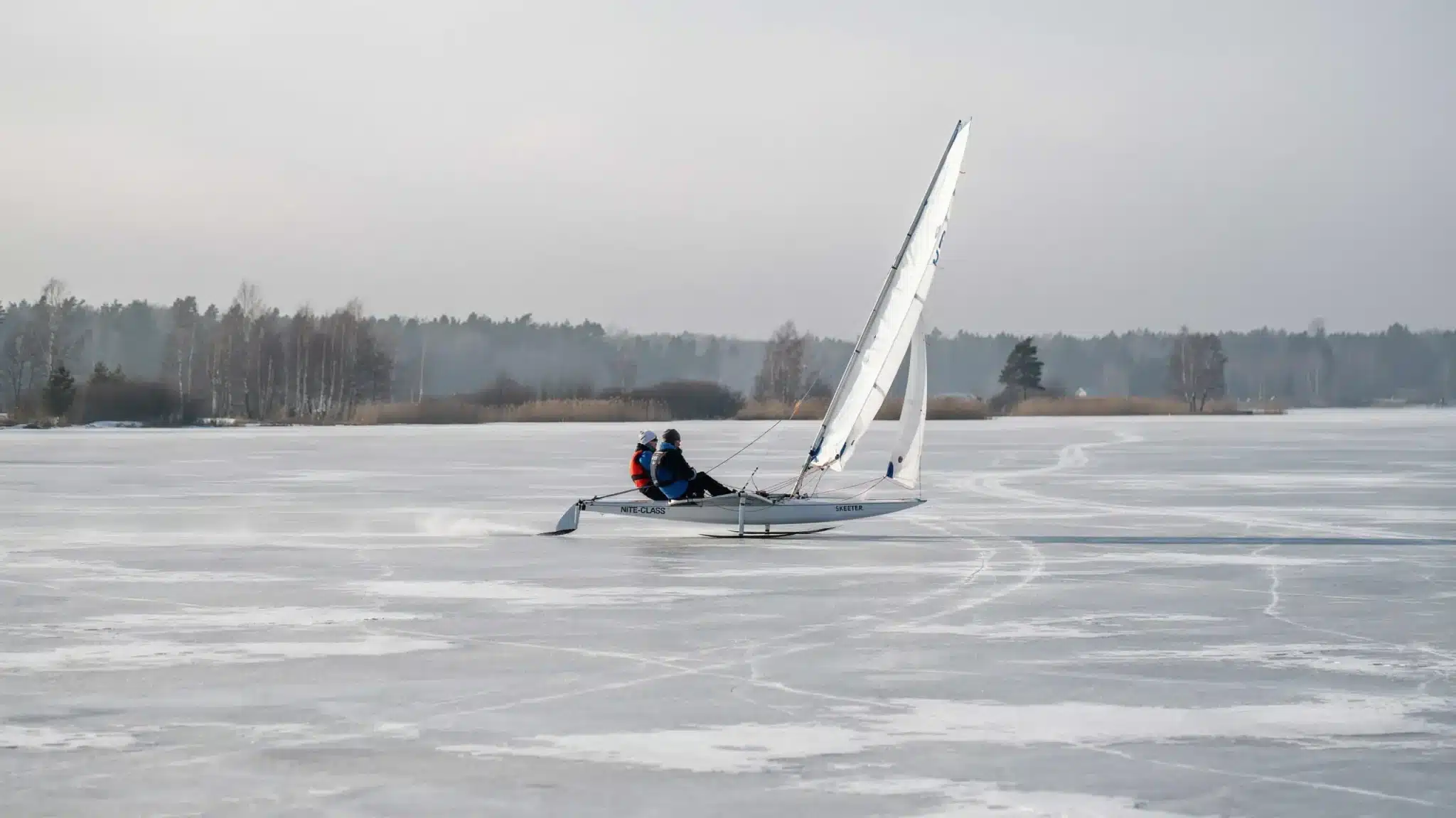 Nite class iceboat sailing across frozen lake with sleek hull and white sail