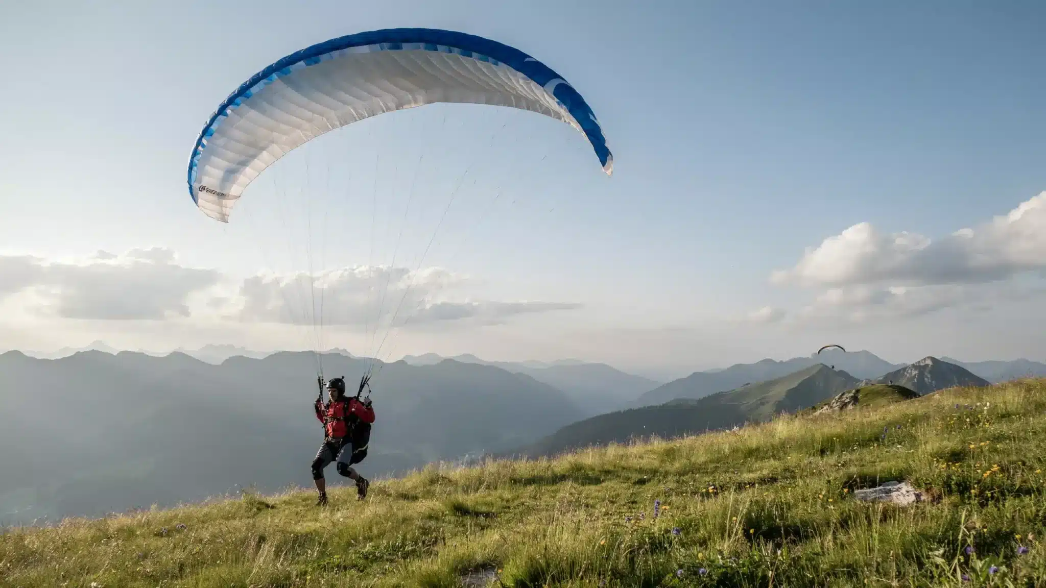 Paraglider flying above green mountain landscape with large wing and clear sky during outdoor flight experience