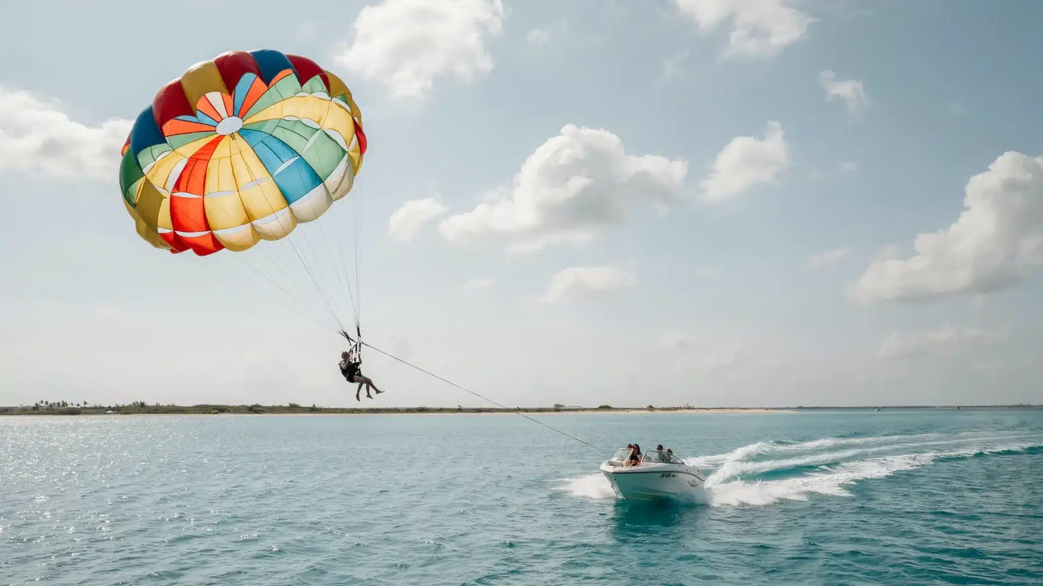 Parasail rider lifted above calm ocean water with colorful canopy and speedboat during coastal adventure activity