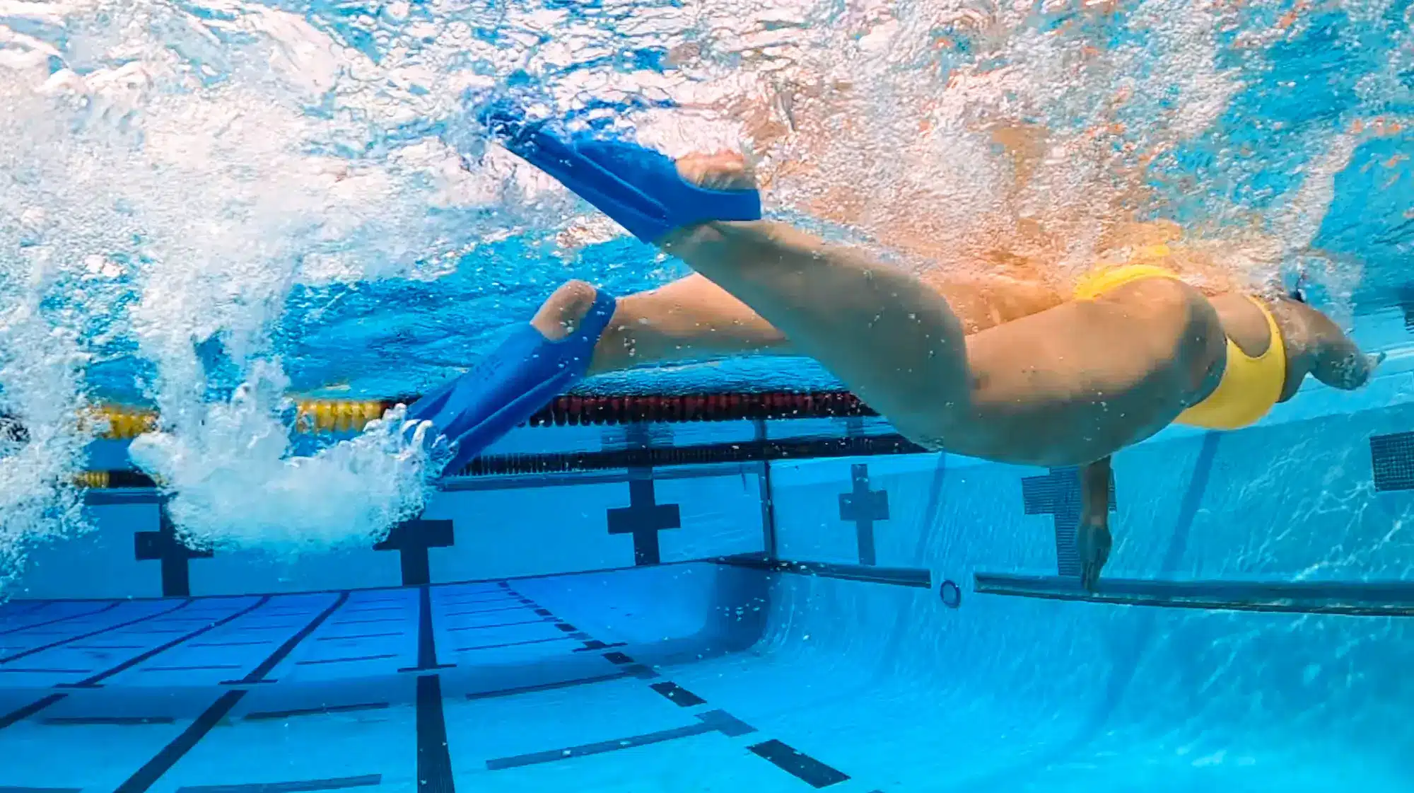 Advanced swimmer using blue fins underwater during an overspeed workout to build faster kicking speed and stronger propulsion