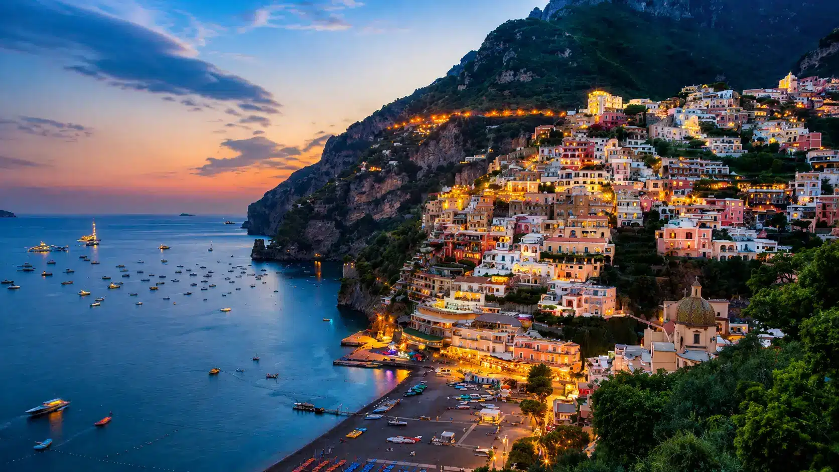 Amalfi Coast surrounded by mountains, pine forests, calm waters, and a traditional sailing boat