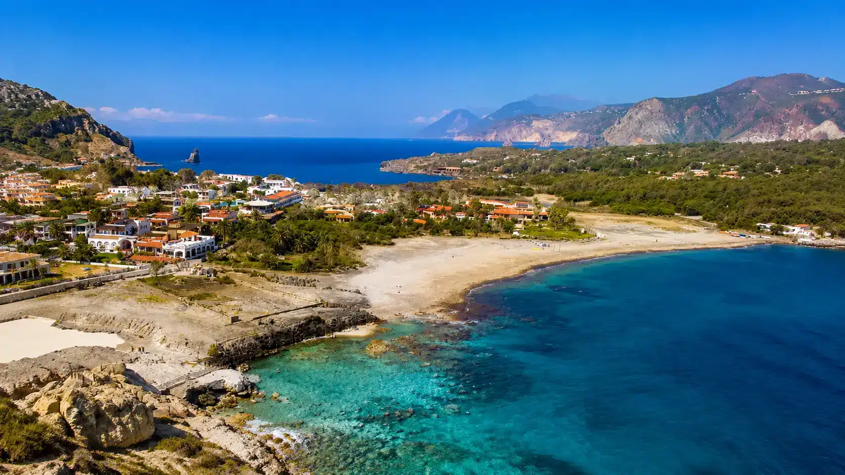 Sicily featuring blue water bay, anchored sailboat, sandy shore, and dramatic mountain backdrop