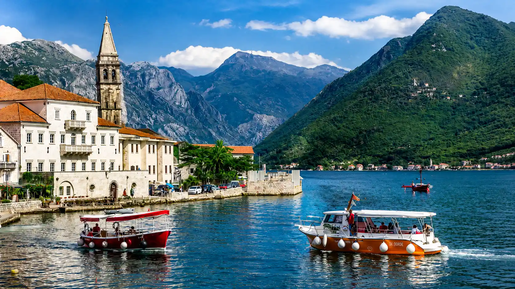 Bay of Kotor with boats, historic stone church, blue water, and green mountains in a scenic seaside landscape