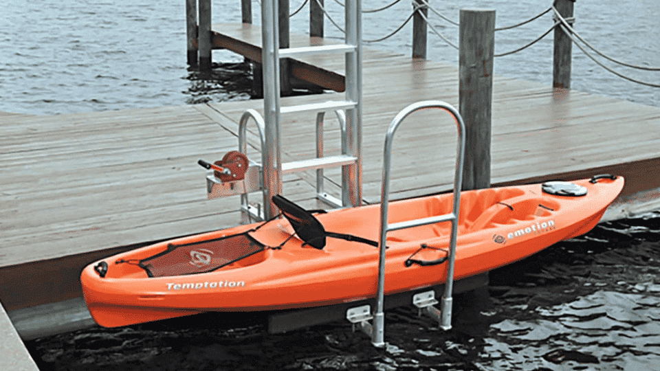 Orange kayak secured to a dock kayak launch system with metal rails on calm water for easy boarding access.