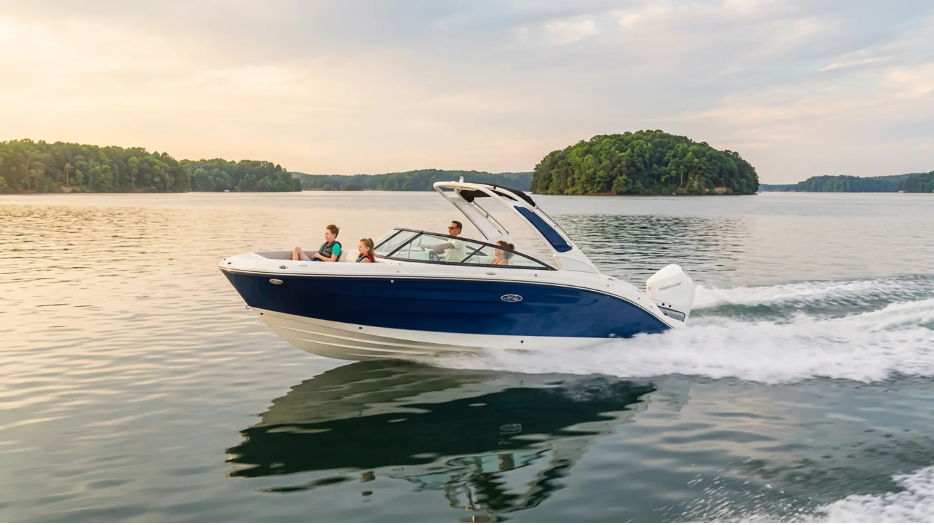 Blue and white deck boat speeding across peaceful lake with passengers and wake trail behind