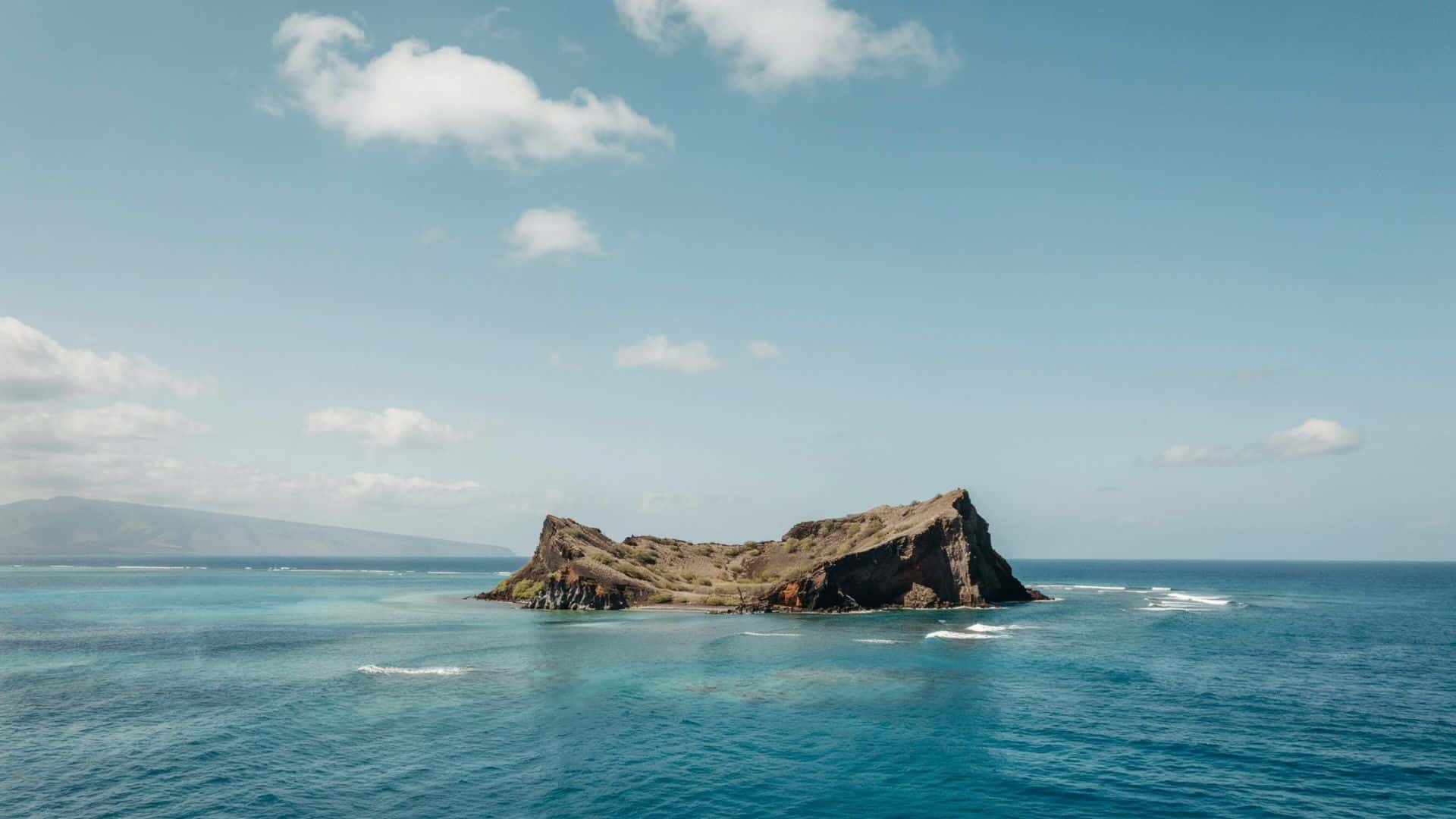 Lehua Crater and Niʻihau island with turquoise ocean waters and a rocky volcanic coastline under a clear blue sky