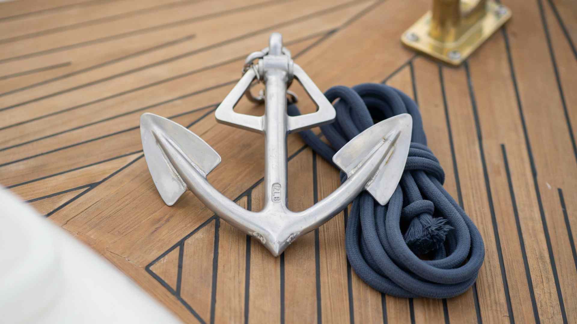 Lightweight fluke anchor with two triangular blades and coiled rope resting on a boat deck in natural daylight