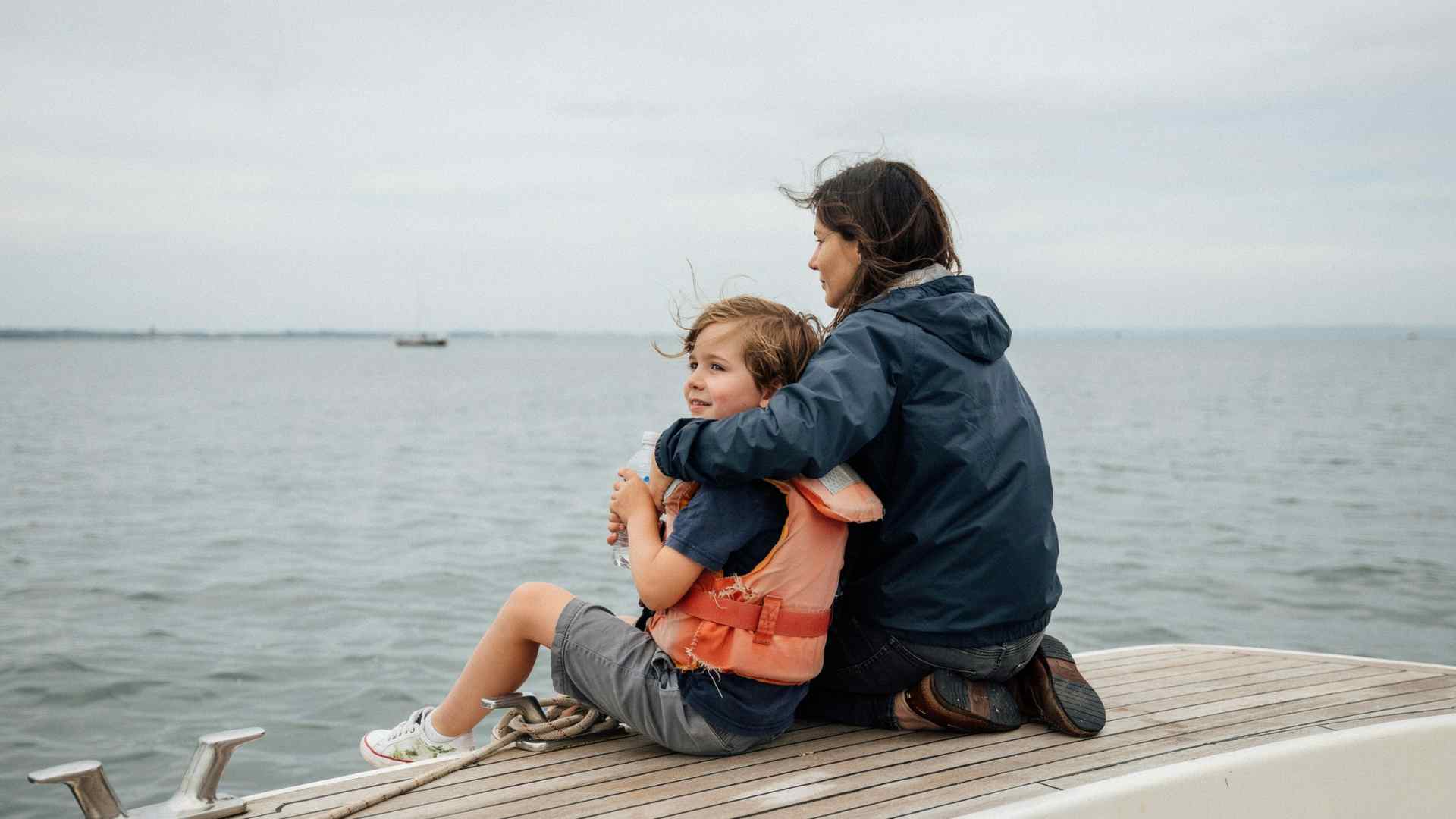 Parent and young child sitting together near the center of a boat deck, facing the horizon