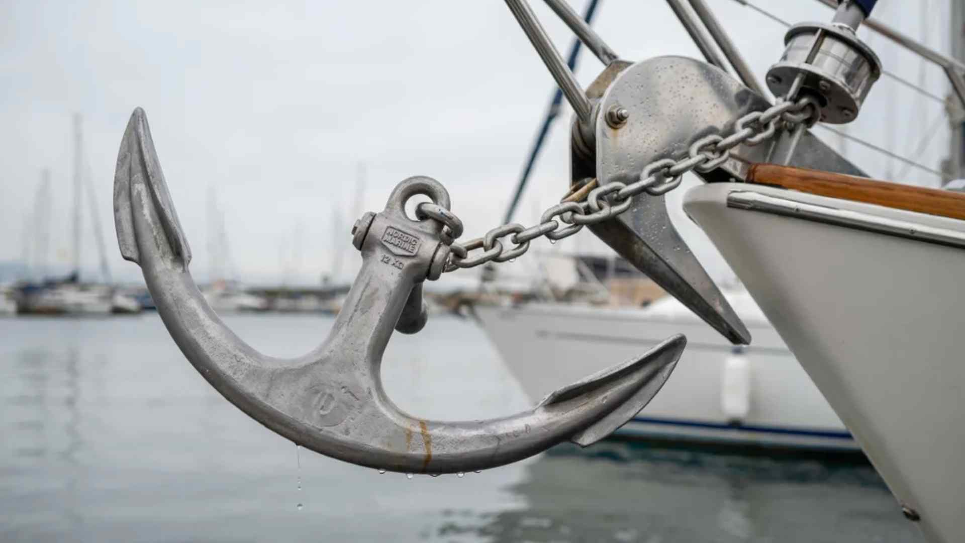 Plow-style anchor with a curved, hinged shank resting on a boat deck beside coiled anchor rope