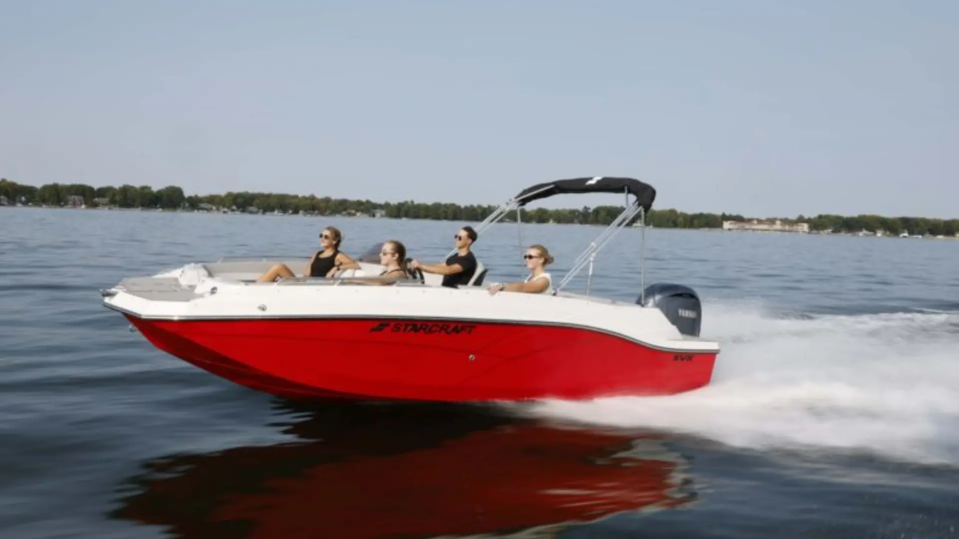 Red and white deck boat moving fast on lake with wake trail and open seating area visible