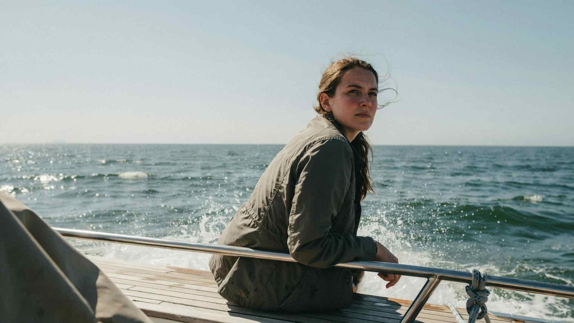 Person sitting low and centered on a boat deck, looking toward the horizon on choppy open water