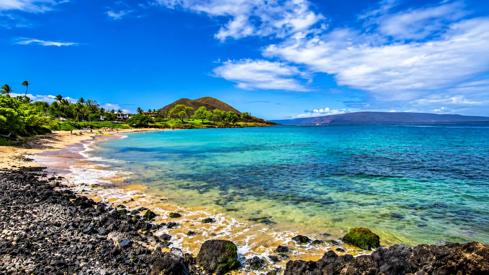 Rocky tropical coast with blue water, coral formations, green hills and clear skies creating a scenic island shoreline