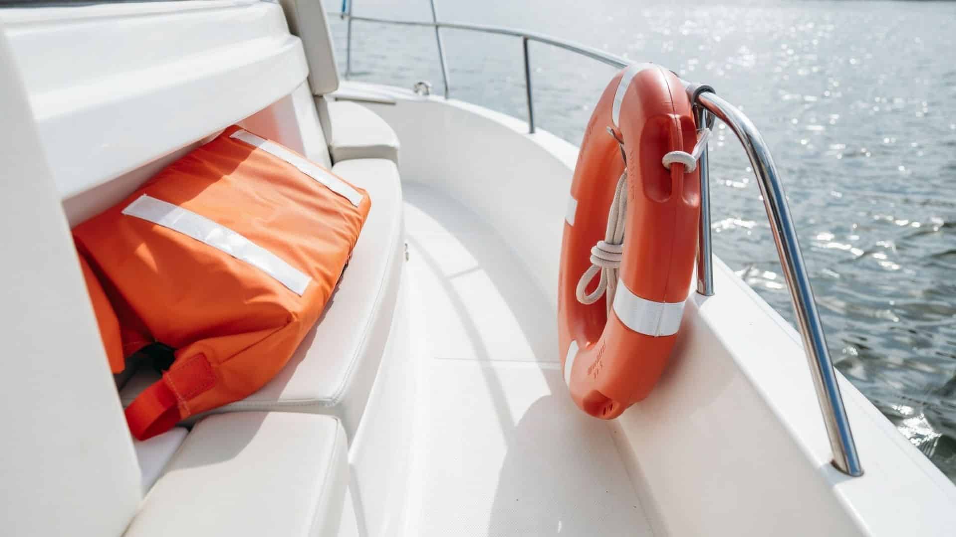 Type IV PFD throwable flotation device resting on a boat deck beside a life ring near the water.