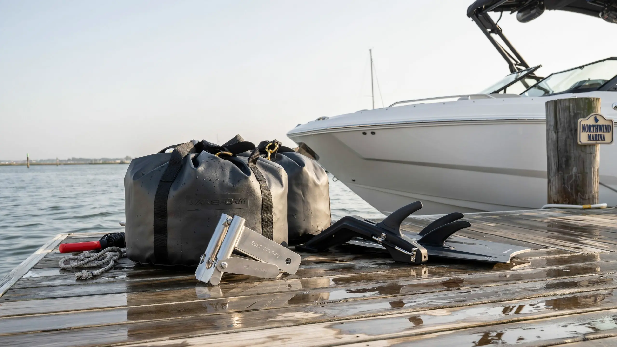 Wake surf gear with ballast bags and surf tabs placed on a wet marina dock beside a white boat for water sports setup