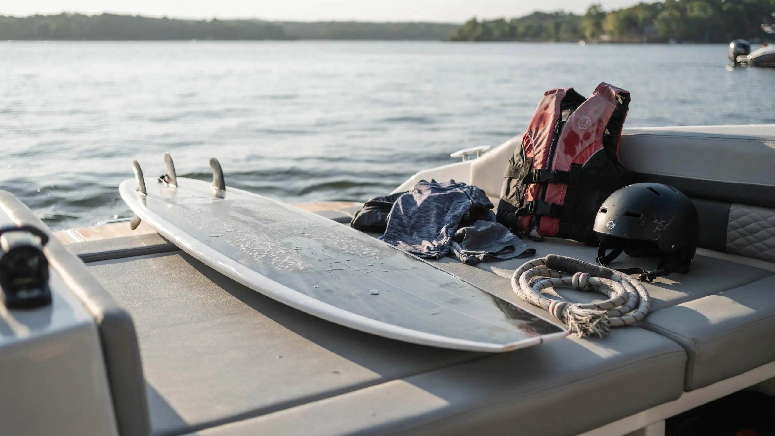 Wakesurfing equipment including board helmet life jacket and rope arranged on a boat deck near lake water
