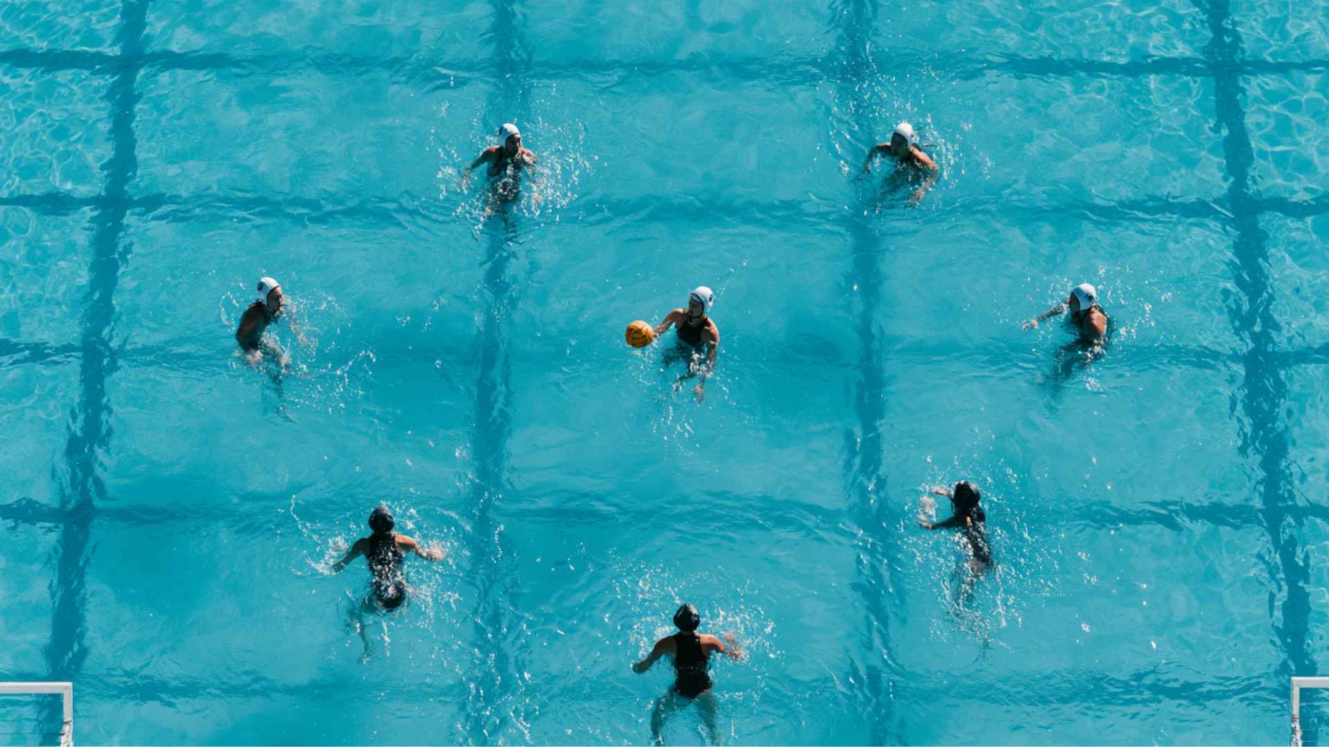 Water polo players run a power play with six attackers passing the ball against five defenders positioned near the goal