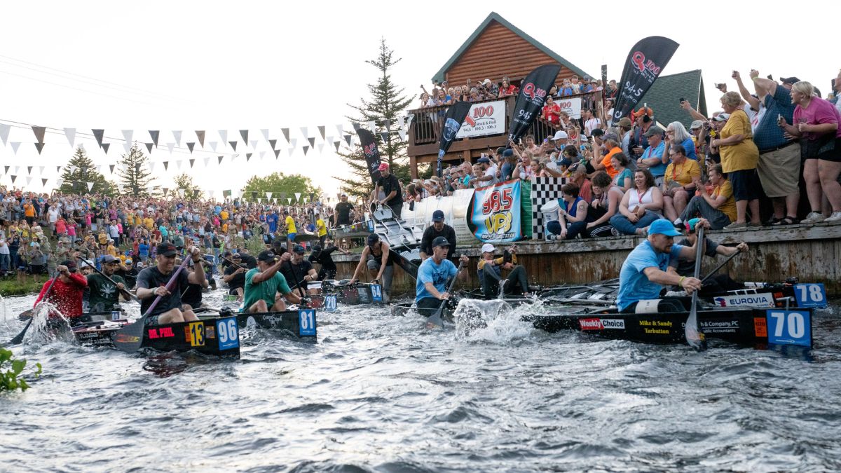 AuSable River Canoe Marathon paddlers racing through the river with spectators watching from the shoreline