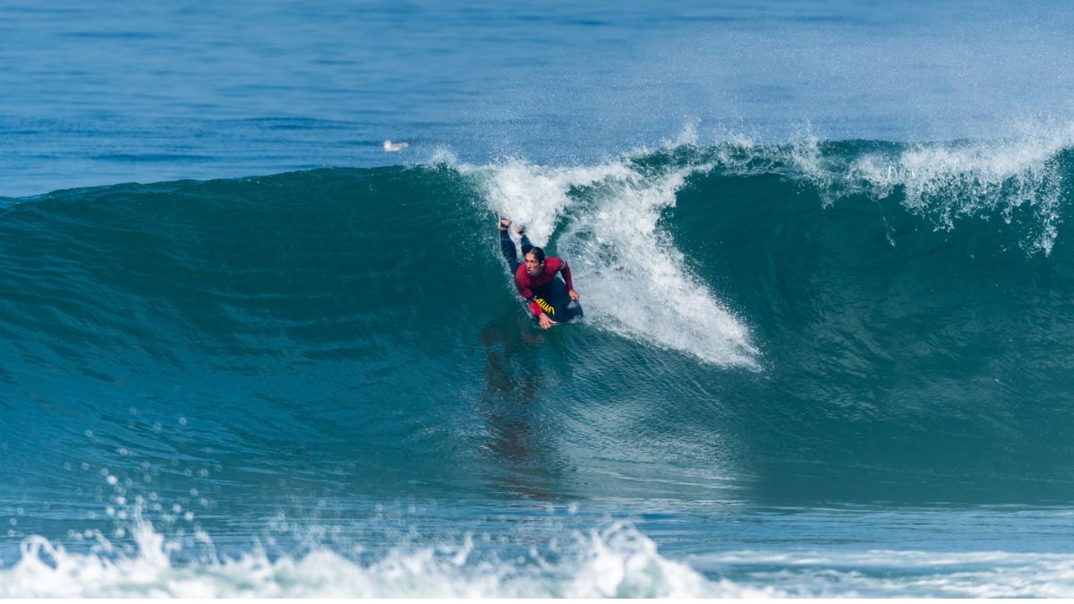 A bodyboarder riding down a large ocean wave with white spray and deep blue water in the background.