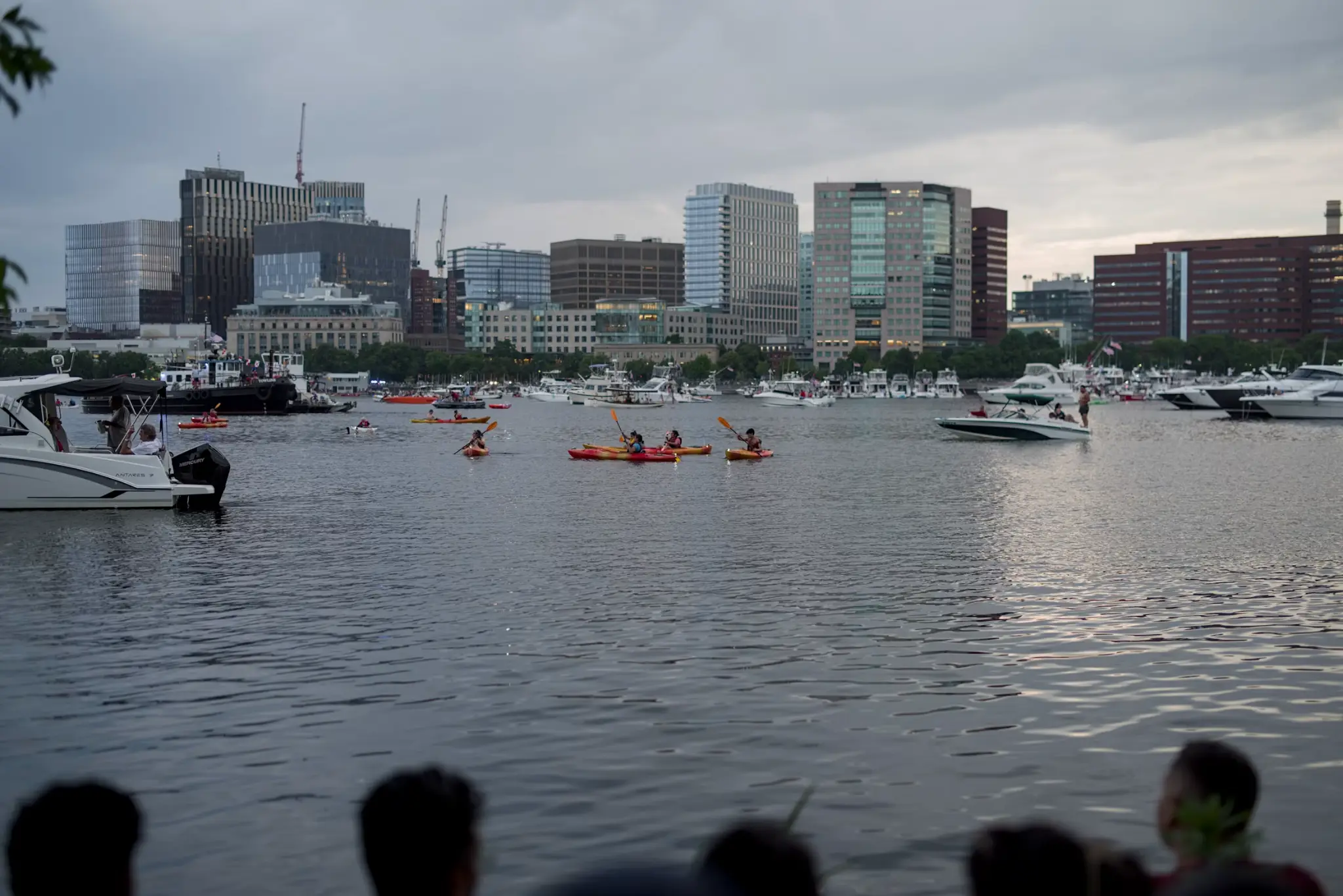 Kayakers paddling on a river with city skyline and boats in the background