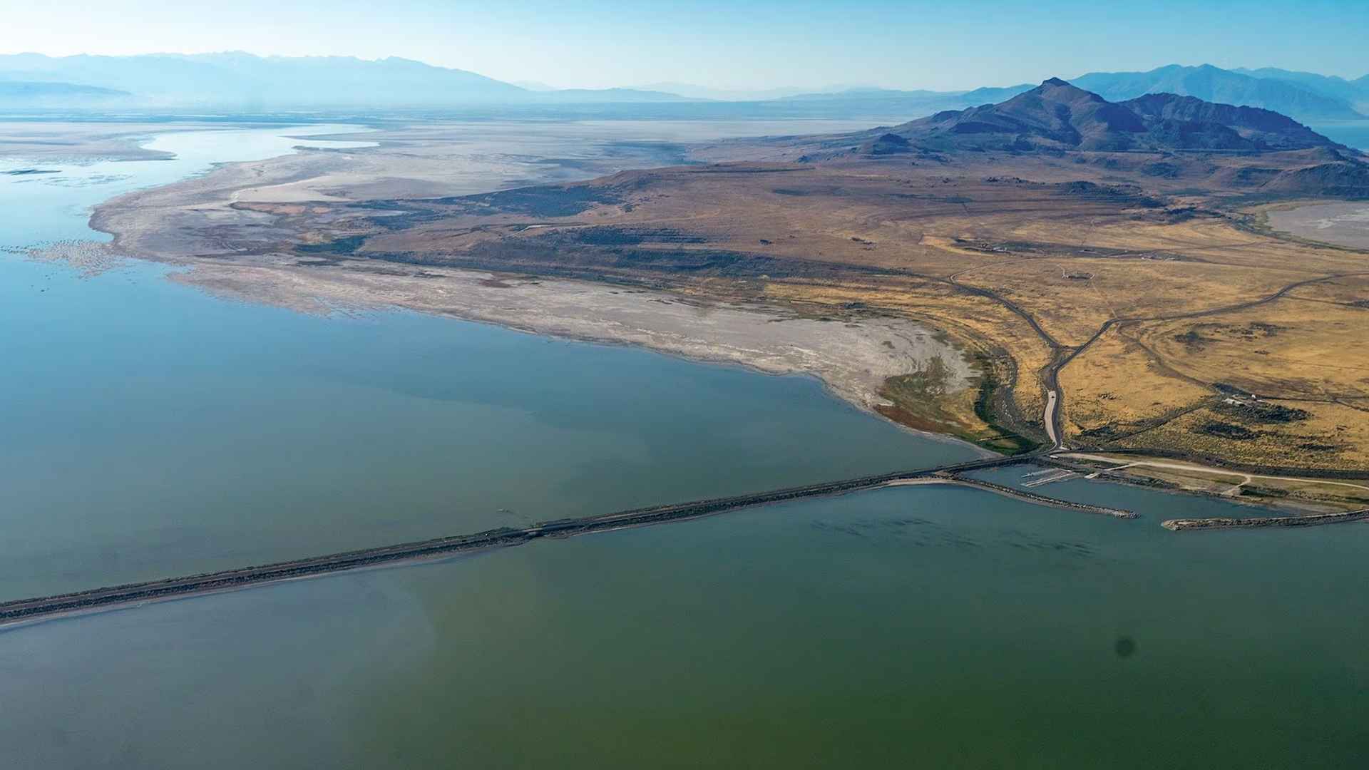Aerial view of Great Salt Lake causeway with exposed lakebed and mountains in the background