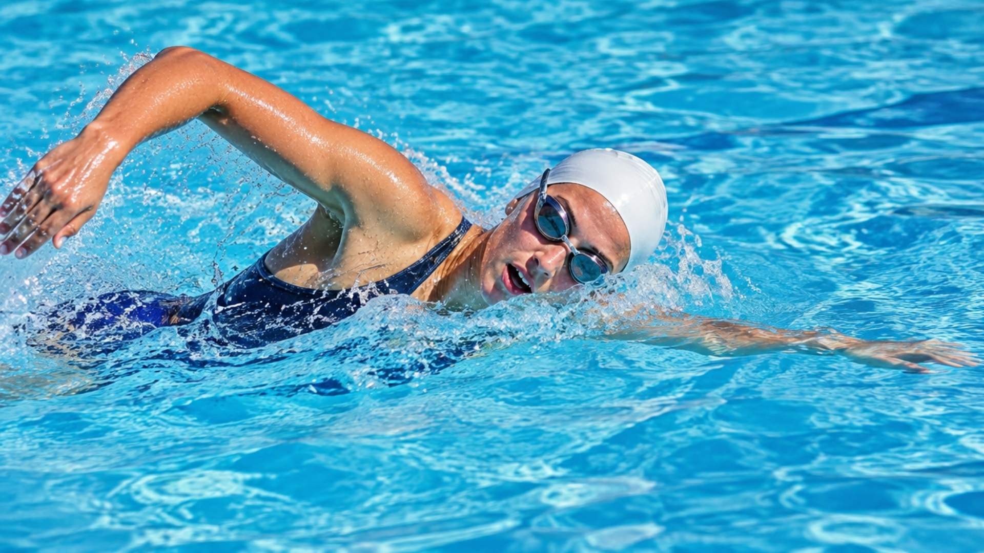 Female swimmer performing freestyle at water level with goggles, swim cap