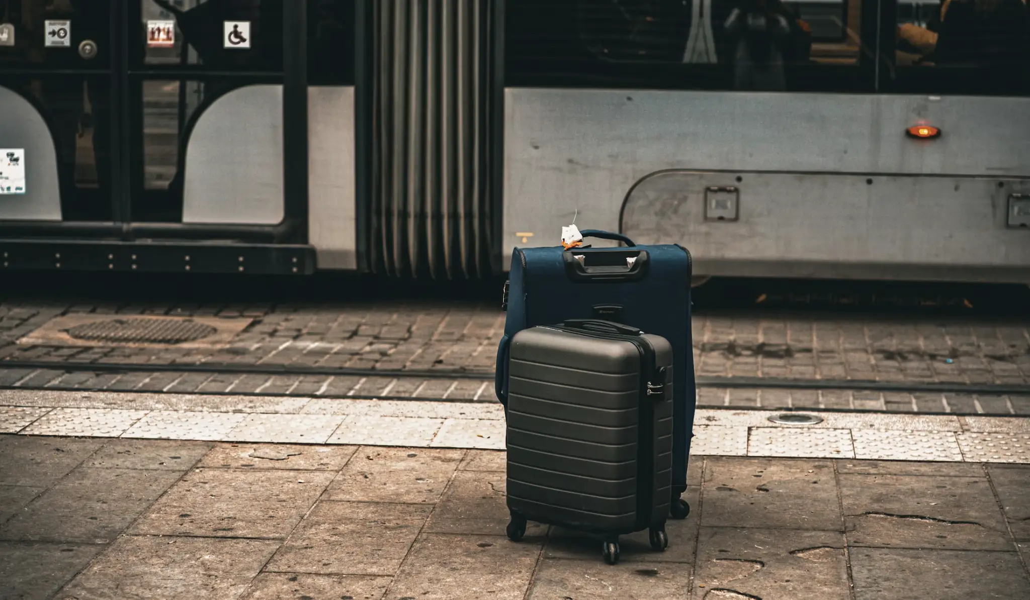 Two suitcases standing on a city street near a parked tram