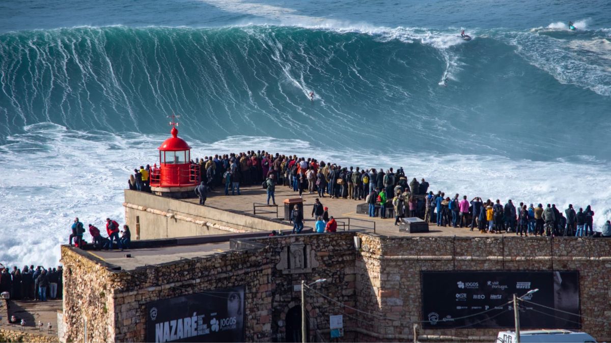 Nazaré big waves at Praia do Norte with surfers riding giant swells and crowds watching from the lighthouse viewpoint