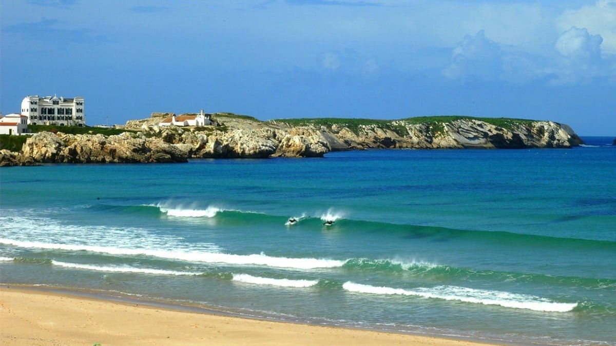 Peniche surf beach with surfers riding Atlantic waves and rocky coastline along Portugal’s peninsula