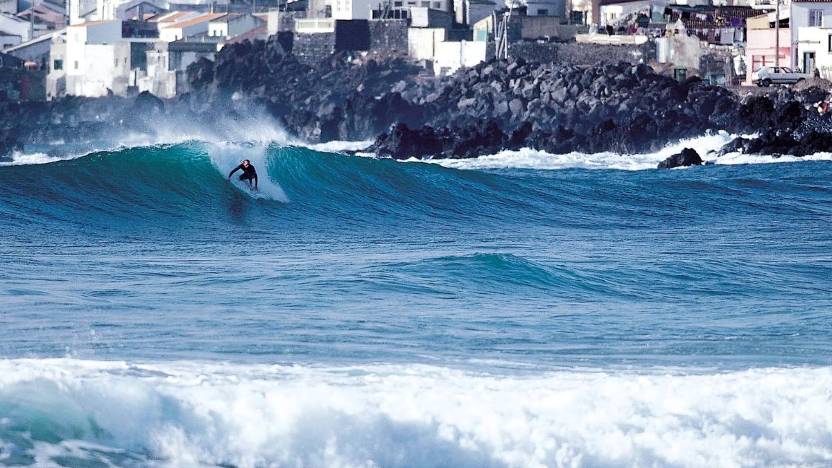 Surfer riding an Atlantic wave near São Miguel in the Azores with rocky coastline and ocean backdrop