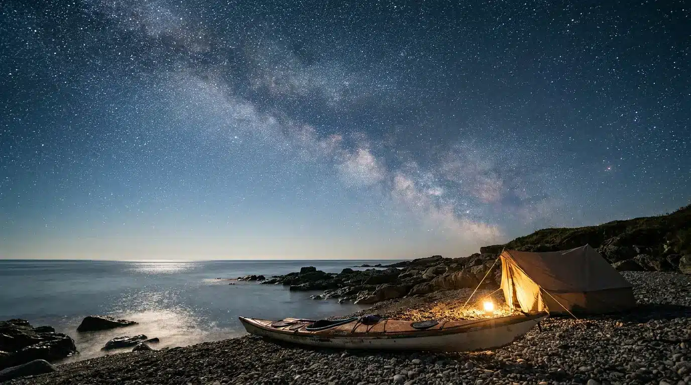 Tent and kayak on rocky beach under starry night sky with Milky Way