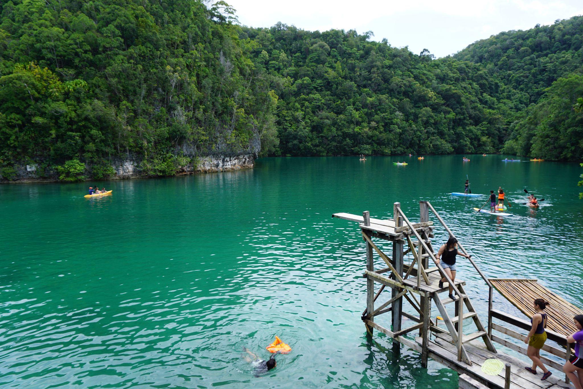People kayaking and swimming in a turquoise lake surrounded by lush green forest