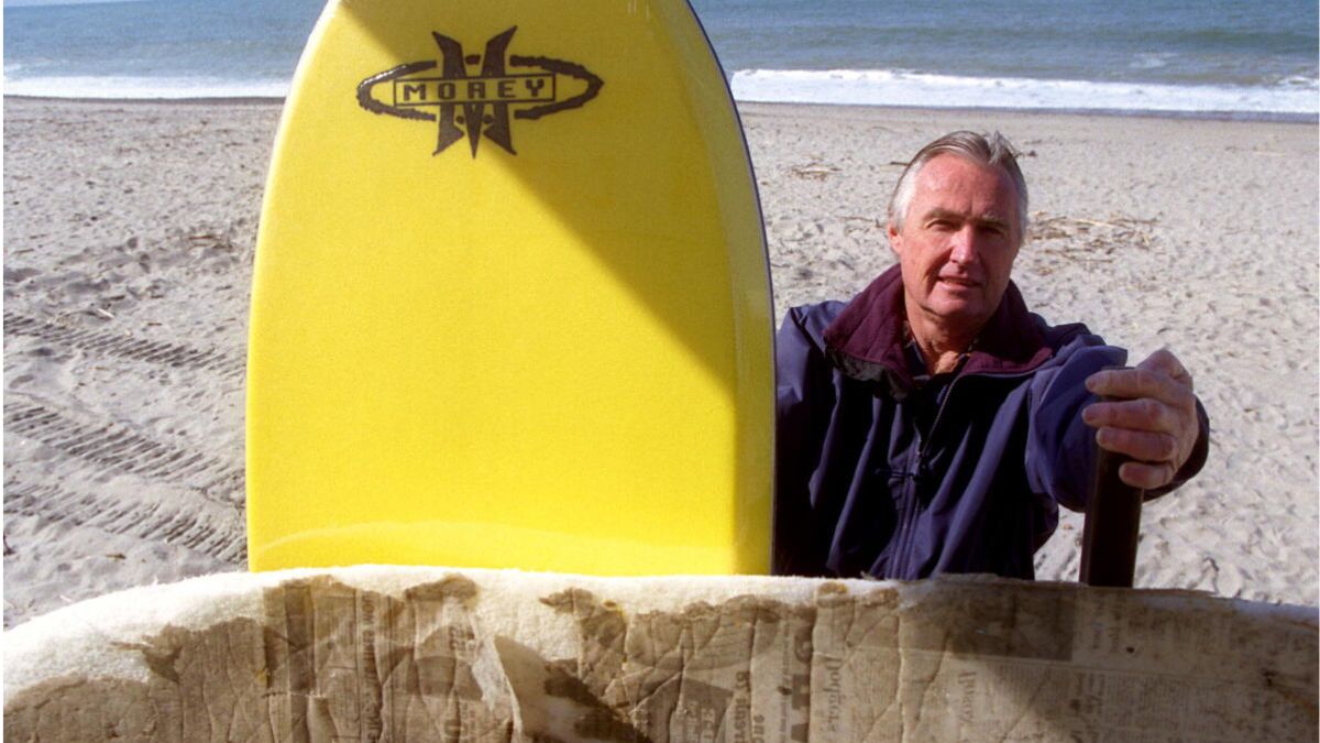 Tom Morey standing beside an early Boogie Board prototype on a beach, showing the origins of modern boogie boarding