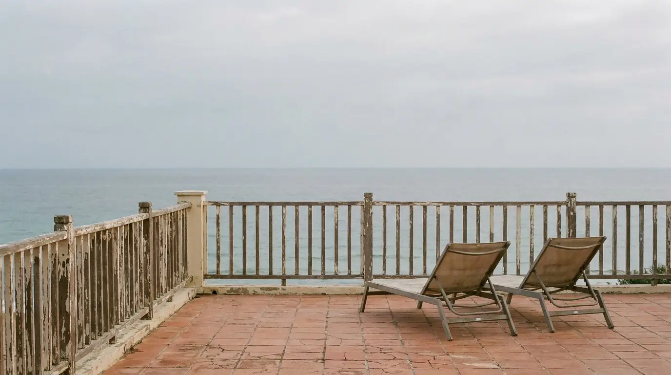 Two lounge chairs on a tiled terrace overlooking the ocean on a cloudy day