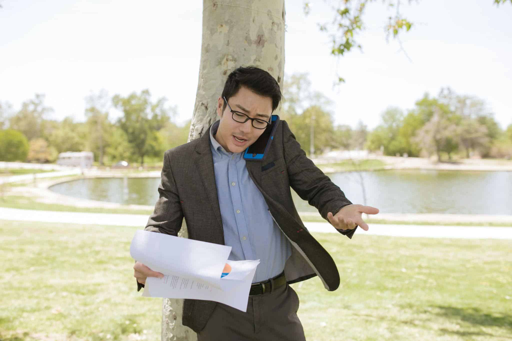 Man in suit multitasking with phone and papers outdoors near a lake