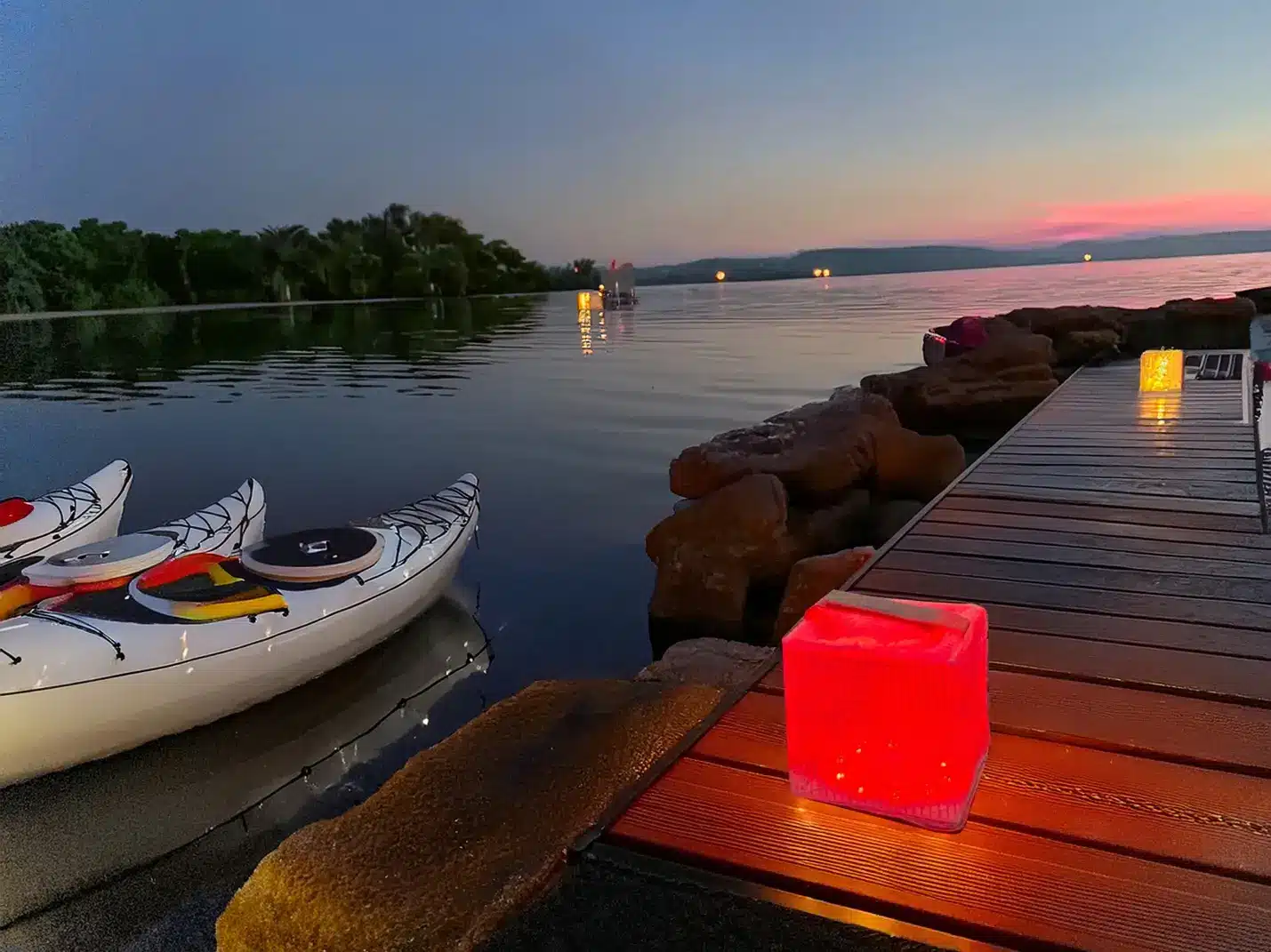 Kayaks docked by a wooden pier with illuminated lanterns during sunset on a calm lake