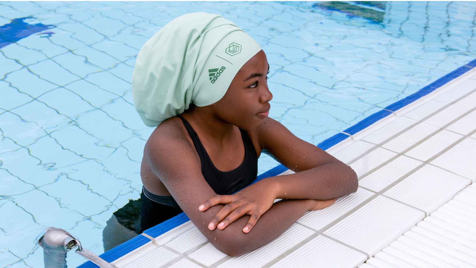 Swimmer wearing a white swim cap resting at the edge of a pool after a swim session