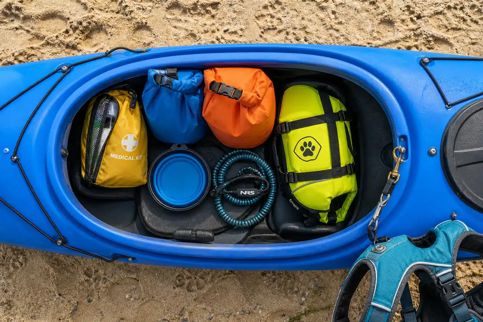 Blue kayak filled with colorful dry bags and gear on sandy beach
