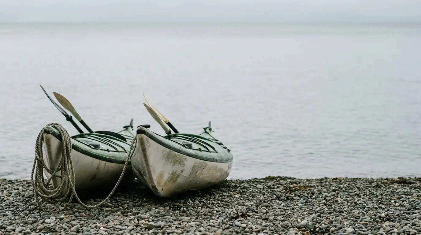 Two kayaks with paddles on a pebble beach facing calm sea waters