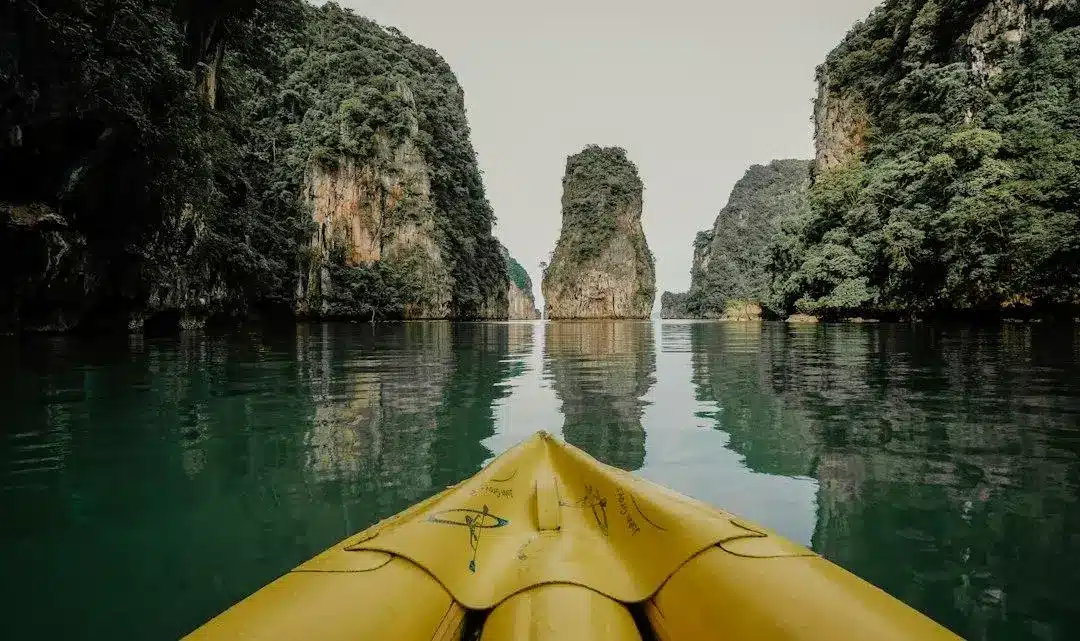 Yellow kayak navigating through calm waters surrounded by towering limestone cliffs and lush greenery